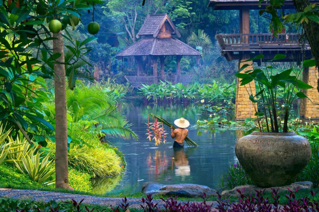 A Thai man in traditional attire carrying flowers through a calm body of water