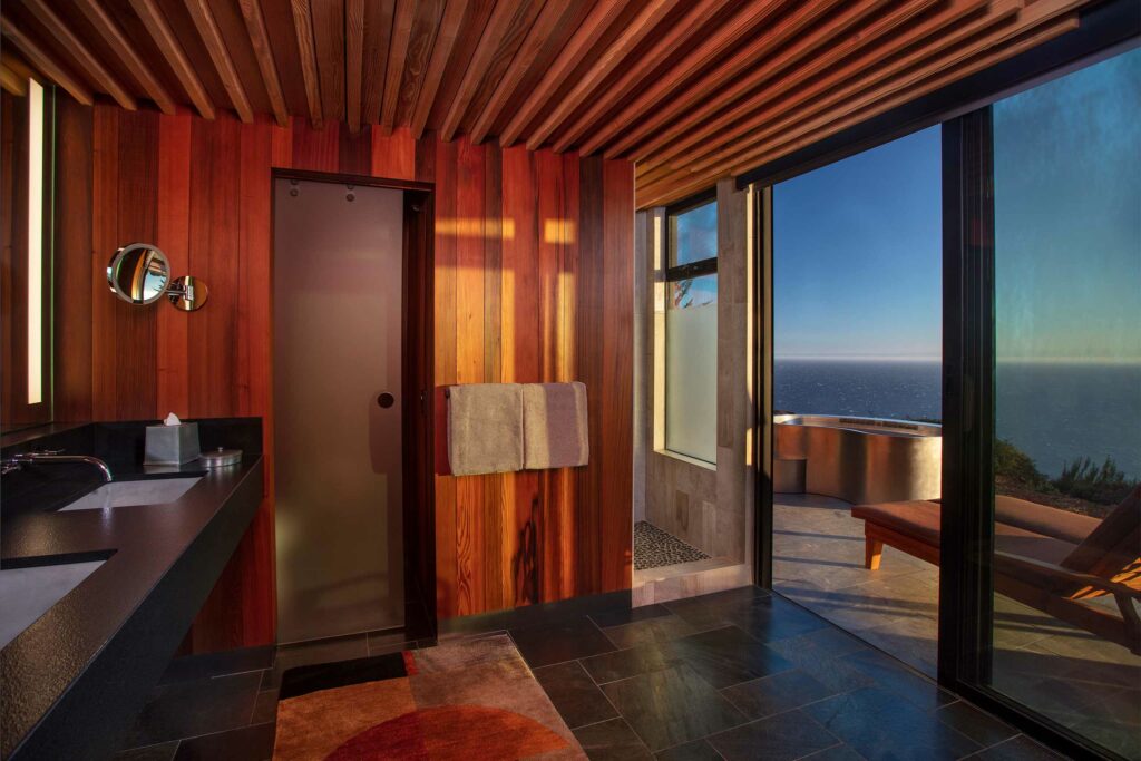 A bathroom with red wood walls and ocean views.