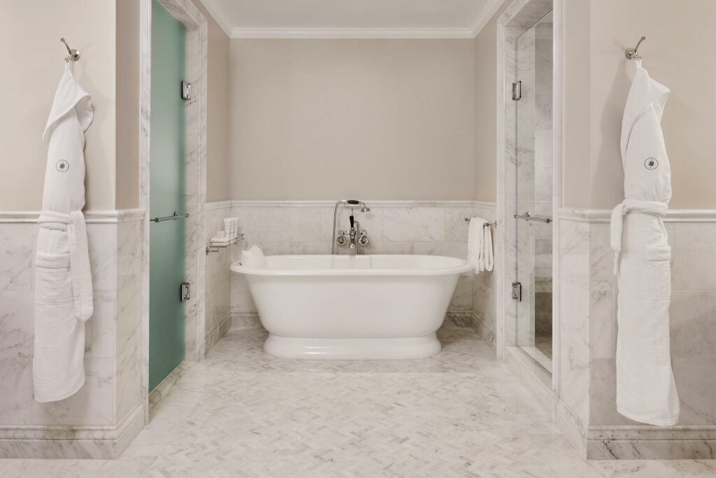 A clean white bathroom with a freestanding bathtub and two white robes at Rosewood Miramar Beach.