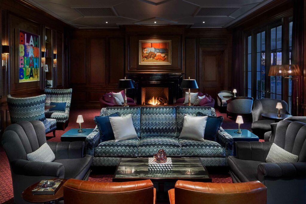 A dimly lit Manor Bar with dark wood furnishing and  a fireplace at Rosewood Miramar Beach.