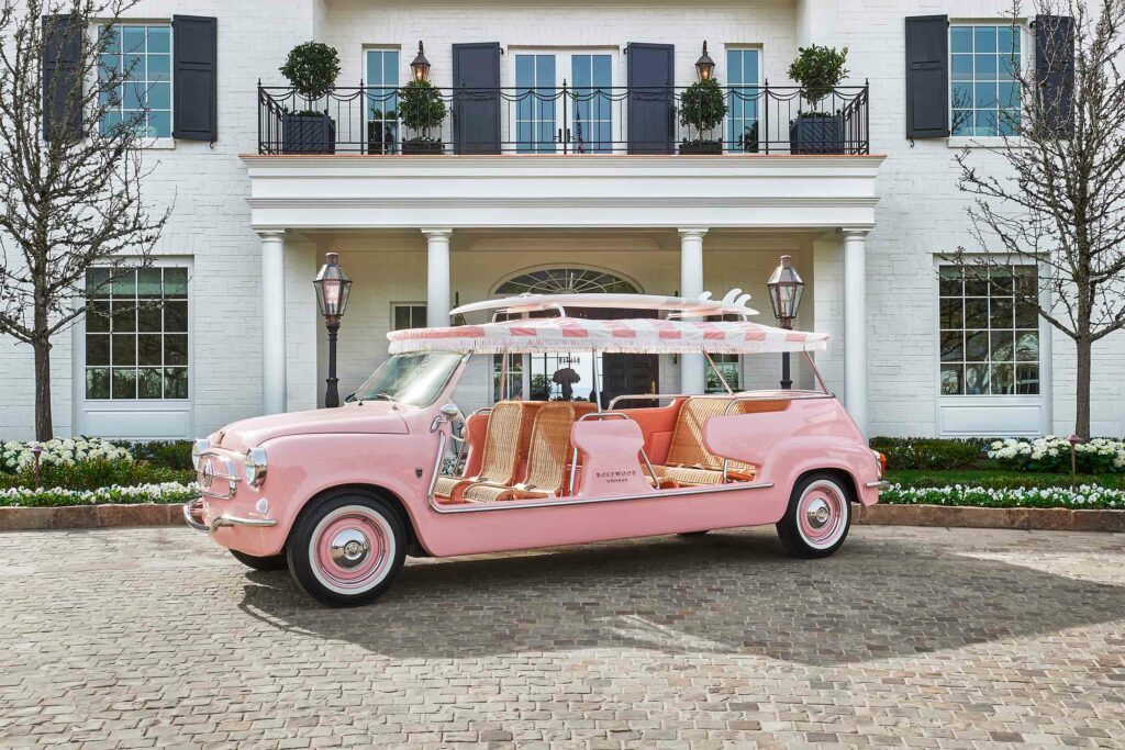 A pink Rosewood buggy parked outside of a white mansion.