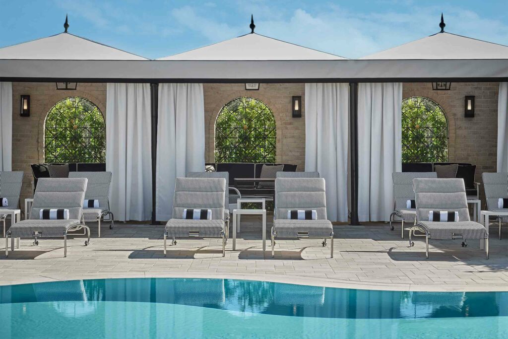 A glistening blue pool with sunloungers and white marquees behind it.