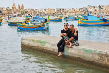 Two friends sitting on the pier at Marsaxlokk in Malta