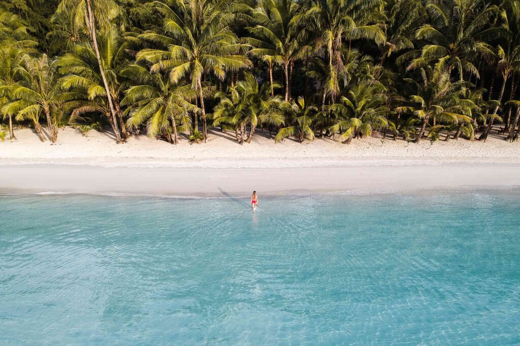 Woman on deserted beach flanked by coconut trees at Soneva Kiri in Thailand