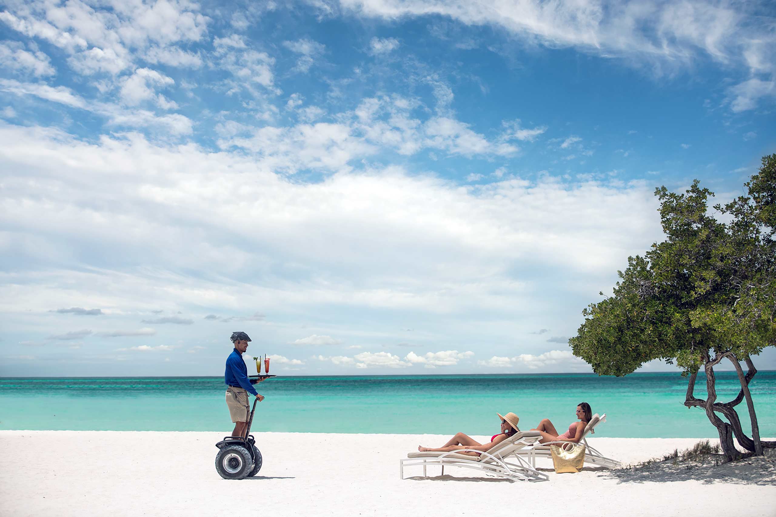 A staff member serves cocktails on a segway by the beach at The Ritz-Carlton Aruba, Noord, Aruba